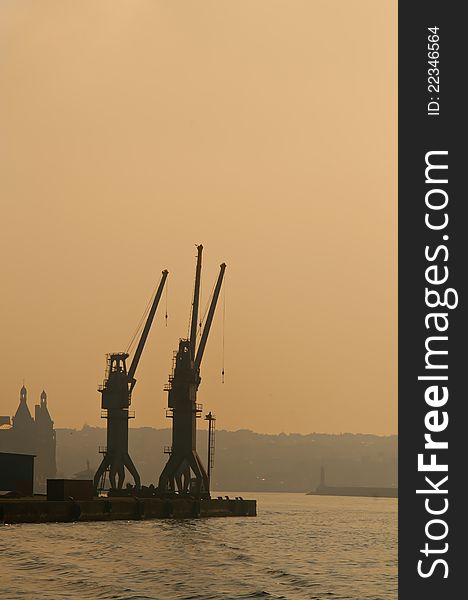 Silhouette of two ship cranes near the sea. They are used for lifting heavy cargos and containers from cargo vessels.