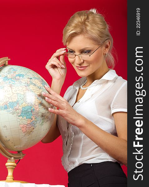 Pretty woman teacher with globe posing in studio on red background