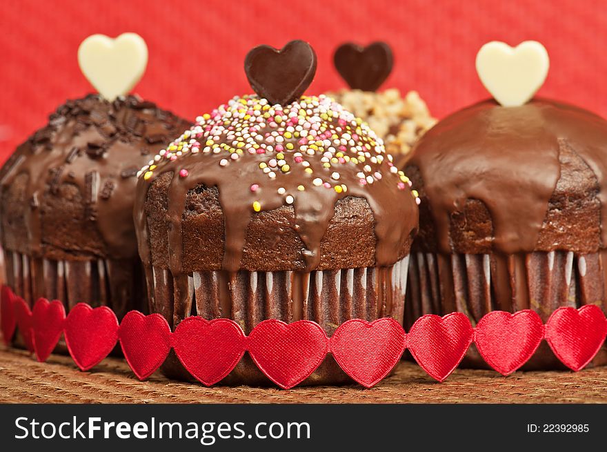 Four Valentine muffins with white and dark chocolate hearts, on wrapped with red fabric hearts