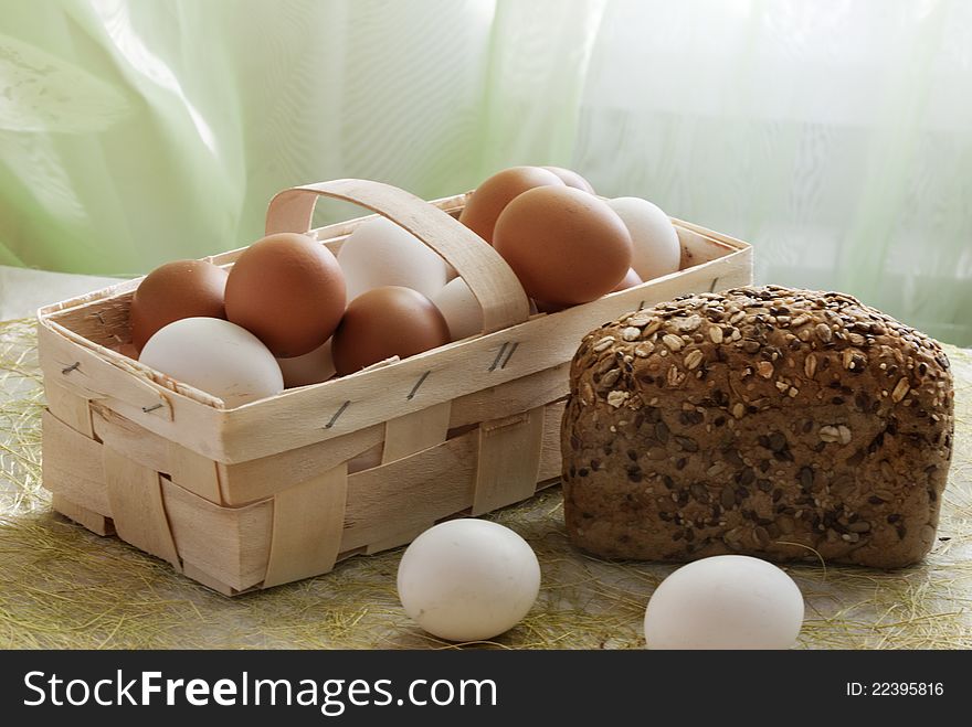 Eggs, yellow both white in a basket and a loaf of rye bread with sunflower seeds. Eggs, yellow both white in a basket and a loaf of rye bread with sunflower seeds
