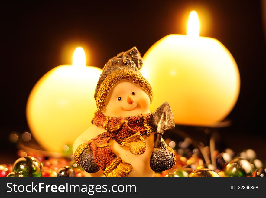 A smiling snowman figurine and burning candles on a black background