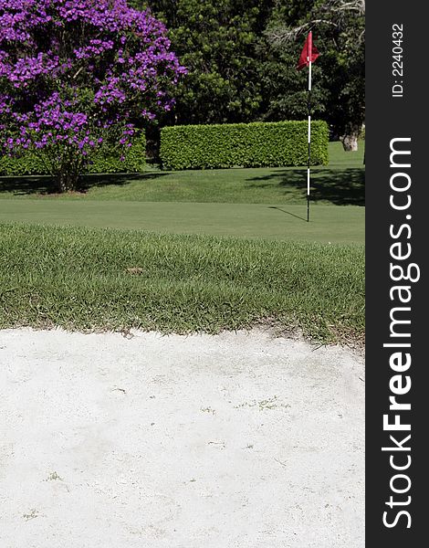 Golf Putting Green With Flag And Sand Bunker In The Foreground. Golf Putting Green With Flag And Sand Bunker In The Foreground