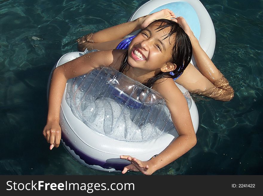 Pretty young girl with a big smile enjoying herself on a floating toy in a swimming pool. Pretty young girl with a big smile enjoying herself on a floating toy in a swimming pool.