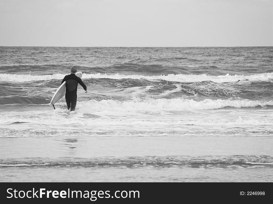 A lone surfer prepares to brave the breakers on an overcast windy day. A lone surfer prepares to brave the breakers on an overcast windy day