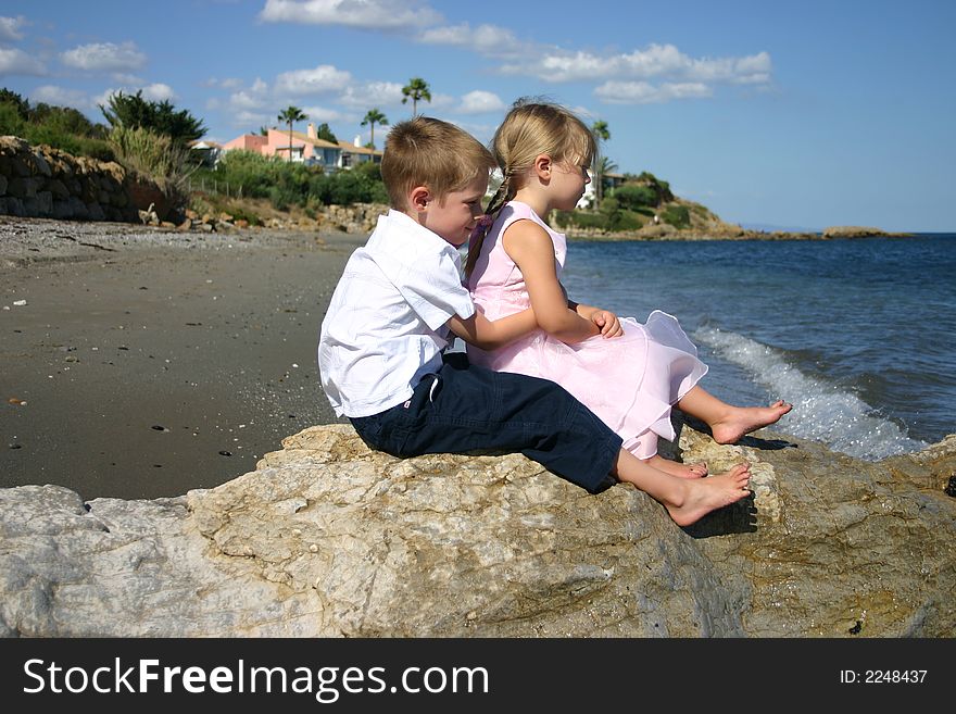 Two young children sat on a rock looking out to sea. Two young children sat on a rock looking out to sea