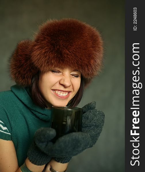 The cheerful girl in a fur cap with a cup of tea