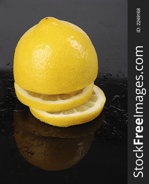 Sliced lemon on black background covered with drops of water.
