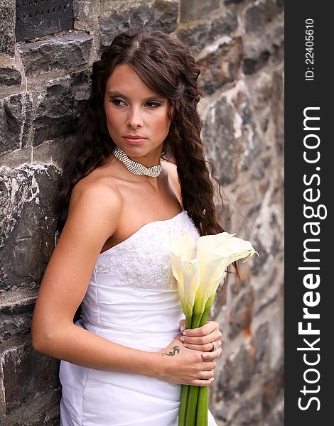 A young bride against an old stone wall holding a bouquet of cream lilies. A young bride against an old stone wall holding a bouquet of cream lilies