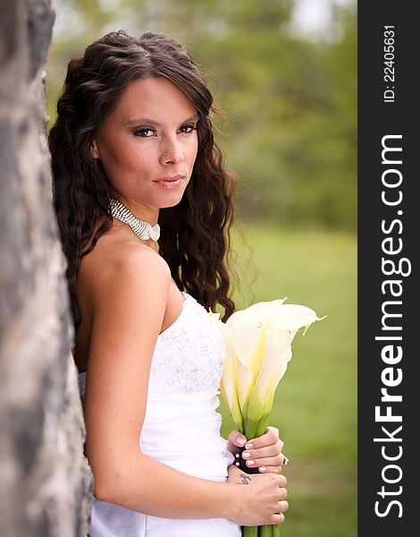 A young bride against an old stone wall holding a bouquet of cream lilies. A young bride against an old stone wall holding a bouquet of cream lilies