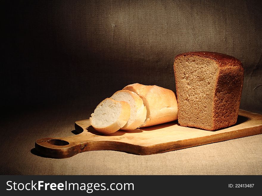 Still life with sliced bread on cutting board under beam of light