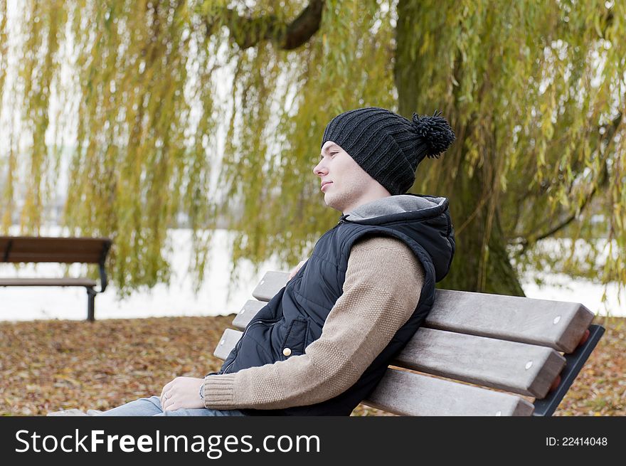 Man sits on the bench in the park on the background of leaves and willow tree