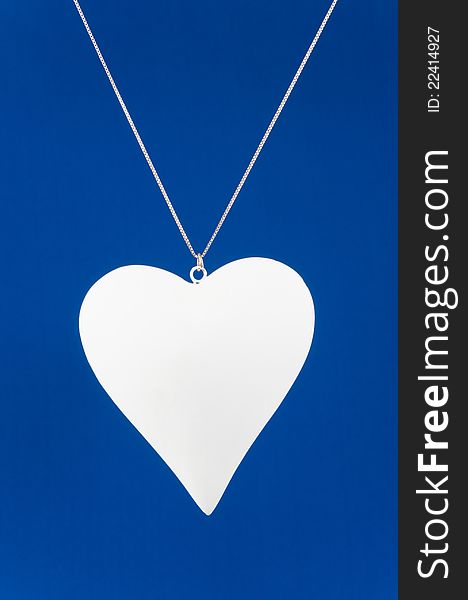 White heart hanging on necklace isolated on blue background. White heart hanging on necklace isolated on blue background
