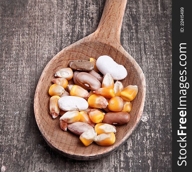 Wooden spoon with beans and corn on wooden plank