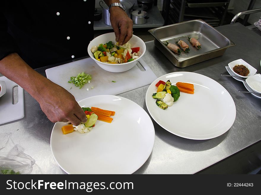 Restaurant kitchen chef preparing a plate with fresh vegetables and garnish. Restaurant kitchen chef preparing a plate with fresh vegetables and garnish