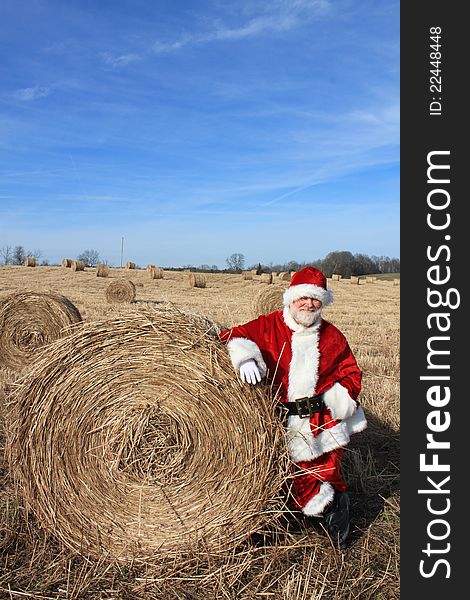 Santa Claus standing against a bale of hay in a hay field. Santa Claus standing against a bale of hay in a hay field.