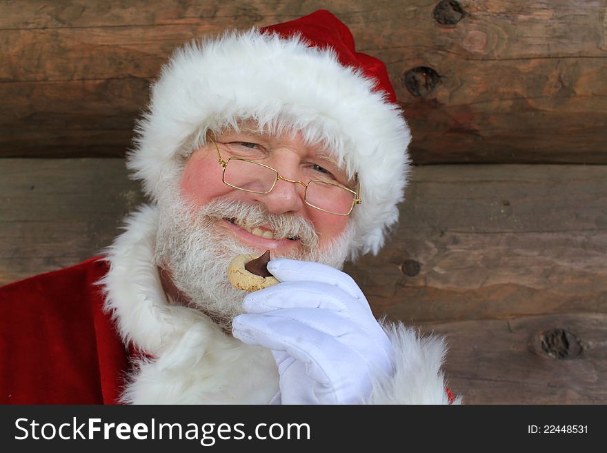 Santa Claus enjoying a traditional Christmas cookie in front of the wall of a log cabin. Santa Claus enjoying a traditional Christmas cookie in front of the wall of a log cabin.