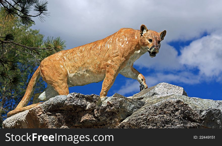 A bronze cast of a cougar perched high atop a rugged rocky mountain. A bronze cast of a cougar perched high atop a rugged rocky mountain.