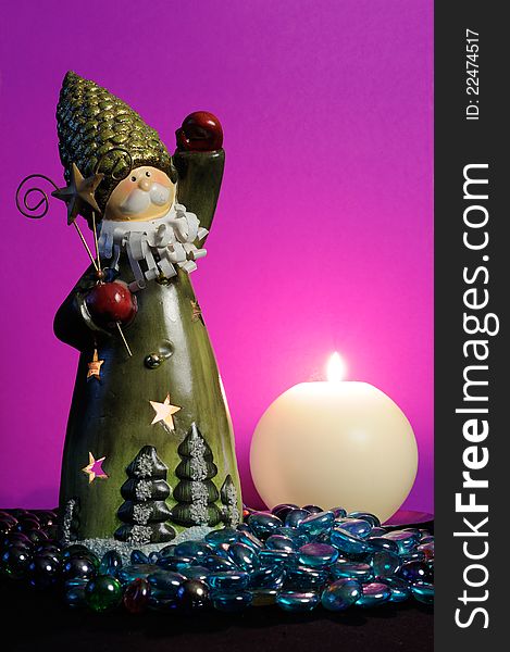 A Santa Claus candlestick and a burning spherical candle with blue glass stones against a magic purple background. A Santa Claus candlestick and a burning spherical candle with blue glass stones against a magic purple background