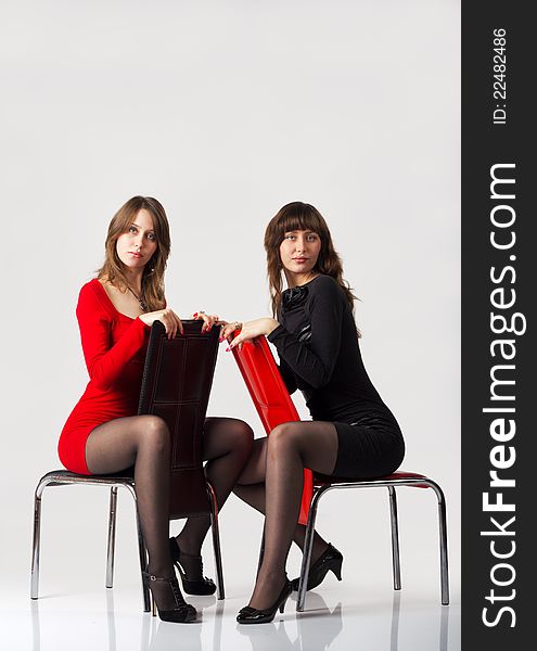 Young pretty sisters twins posing sitting in studio on light background