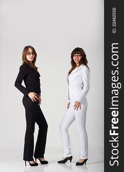 Young pretty sisters twins in black and white costumes in studio on light background