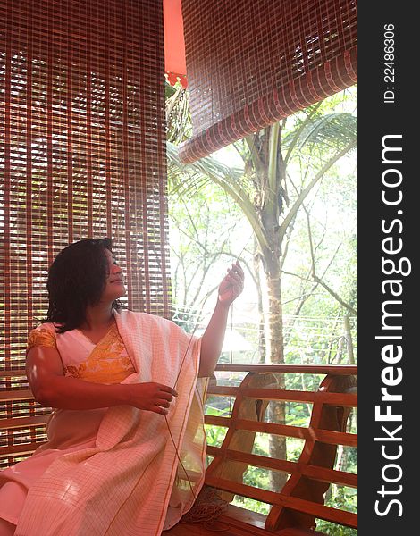 Beautiful Indian Girl Raising Bamboo Curtain from her balcony to have a clear look outside.