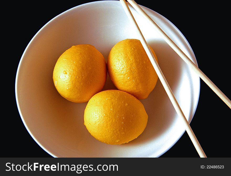 Three lemons in a bowl with chopsticks