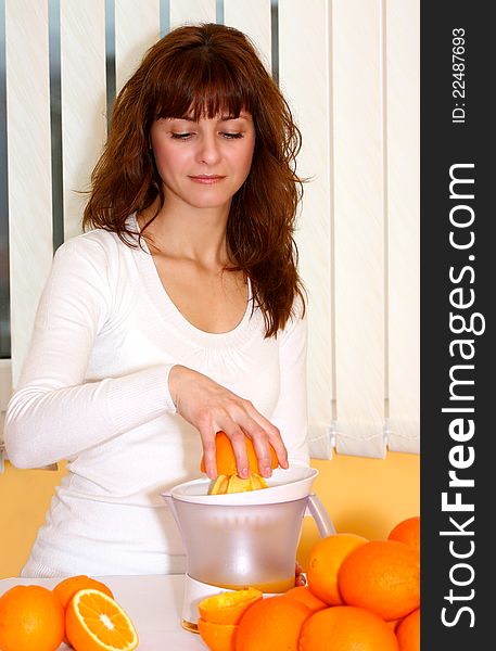 A smiling beautiful woman making fresh orange juice indoor. A smiling beautiful woman making fresh orange juice indoor