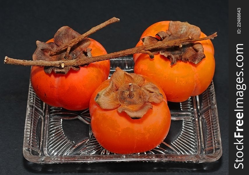 Persimmons in glass dish on a black background