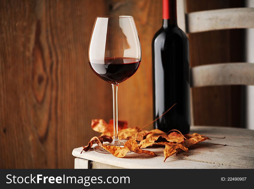 Glass of red wine on a wooden chair, with dry leaves and a bottle of red wine on background
