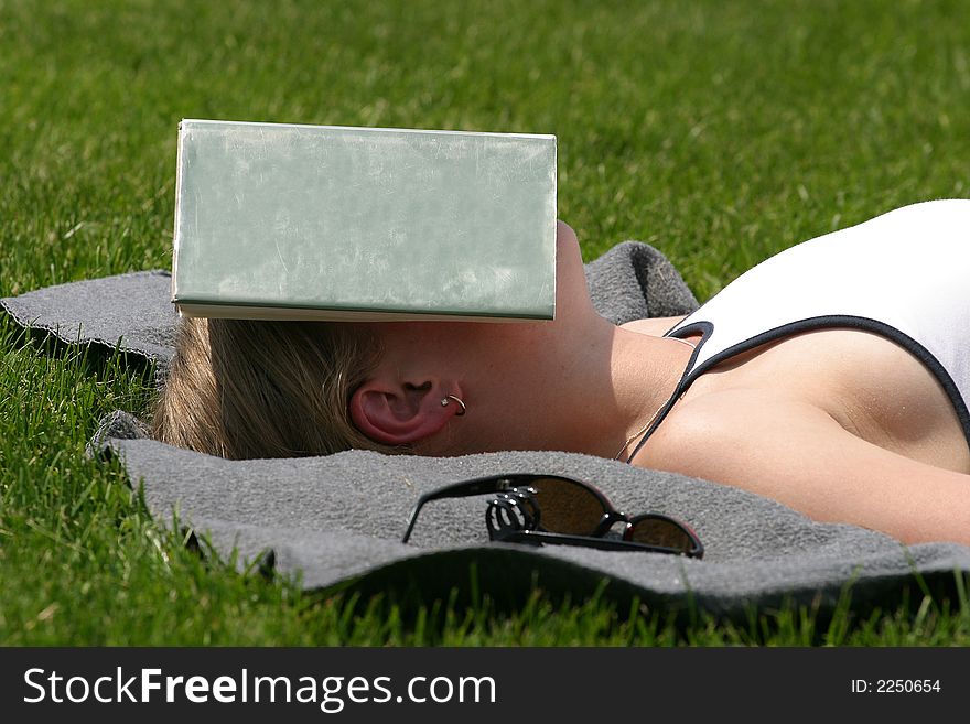A young woman sleeps in the sun with a book over her have to shade her from the sun. A young woman sleeps in the sun with a book over her have to shade her from the sun.