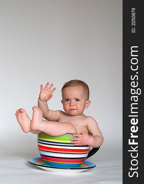 Image of an adorable baby sitting in a colorful, over-sized teacup. Image of an adorable baby sitting in a colorful, over-sized teacup