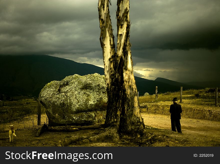 A traditional colombian farmer and his dog walk past a large rock and tree in the imposing colombian countryside with huge mountains and a turbulent sky in the background. A traditional colombian farmer and his dog walk past a large rock and tree in the imposing colombian countryside with huge mountains and a turbulent sky in the background.