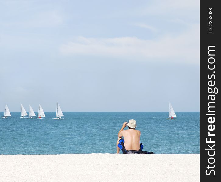 Man sitting on the beach taking photos of sailboats. Man sitting on the beach taking photos of sailboats