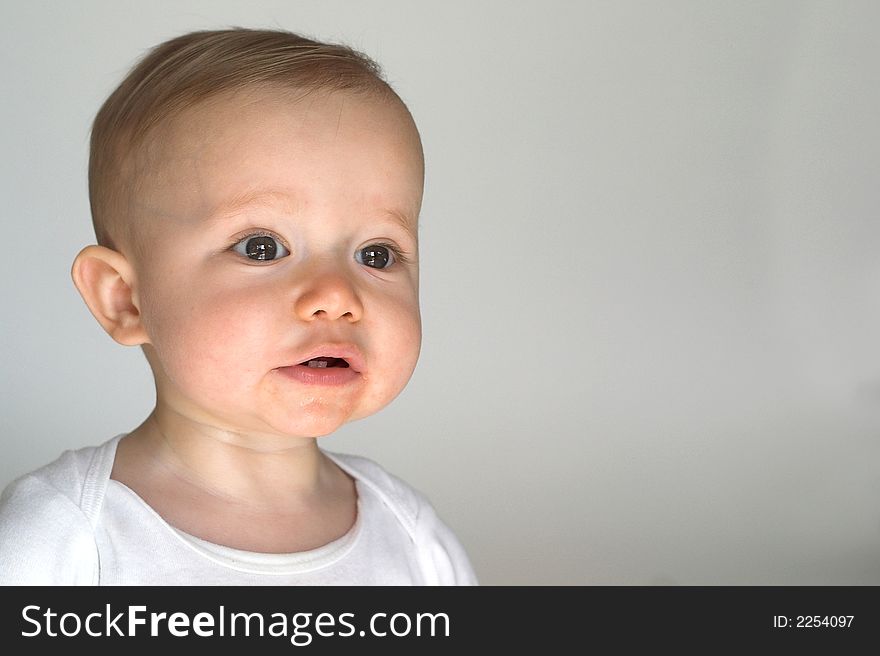 Image of a happy, smiling beautiful baby wearing a white shirt, sitting in front of a white background. Image of a happy, smiling beautiful baby wearing a white shirt, sitting in front of a white background
