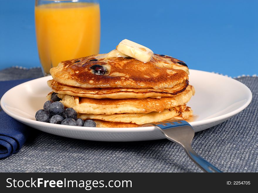 A stack of blueberry pancakes with maple syrup and orange juice. A stack of blueberry pancakes with maple syrup and orange juice