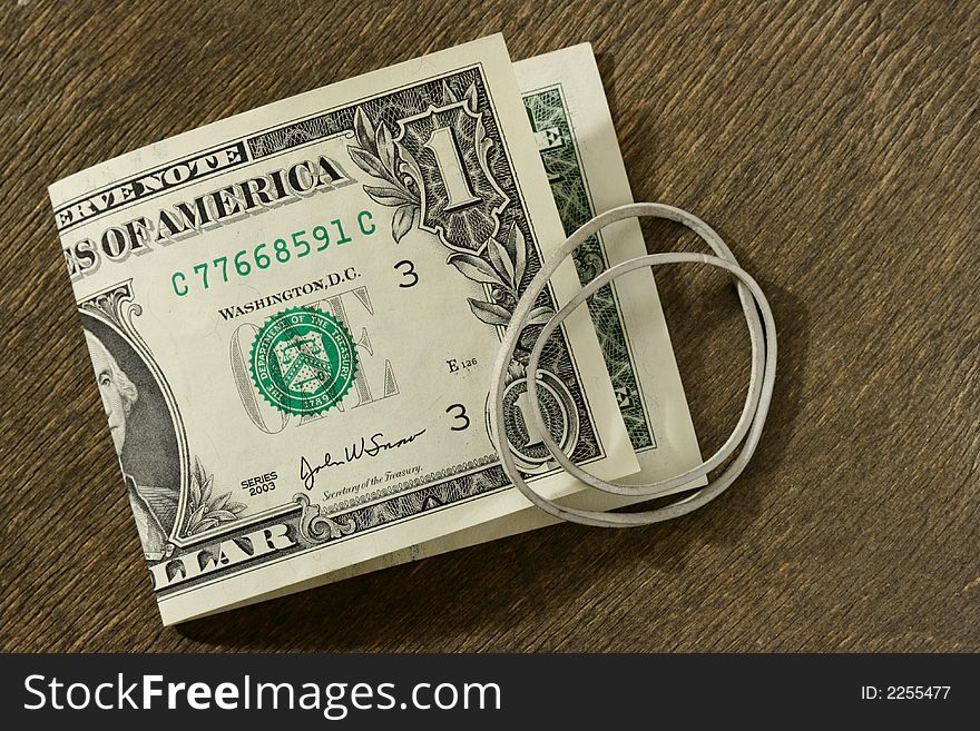 Dollar bill and rubber ring over dark wooden background. Dollar bill and rubber ring over dark wooden background