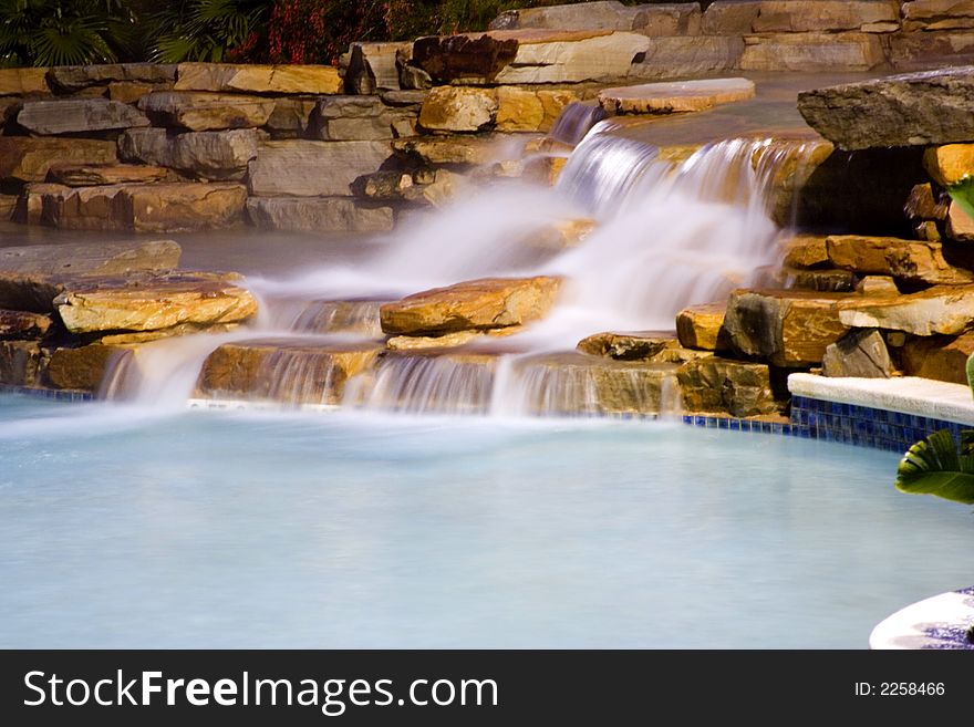 Long exposure of water falls entering a rocky vacation resort pool at night. Long exposure of water falls entering a rocky vacation resort pool at night