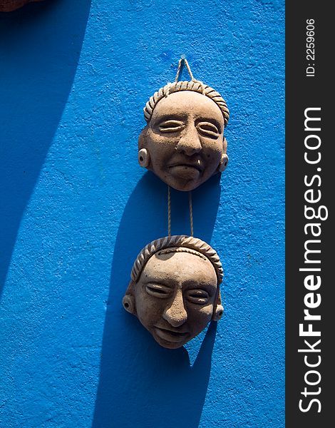 Two small ceramic masks hanging on a bright blue wall. Two small ceramic masks hanging on a bright blue wall