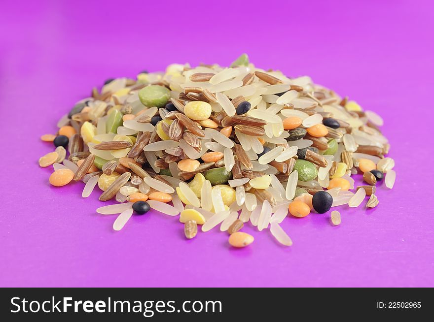 A pile of whole grains & beans mix (red and parboiled rice, split peas and lentils) on a purple background. A pile of whole grains & beans mix (red and parboiled rice, split peas and lentils) on a purple background