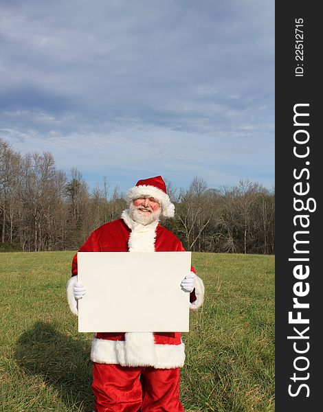 Santa Claus standing in a field holding a big white blank sign. Santa Claus standing in a field holding a big white blank sign.