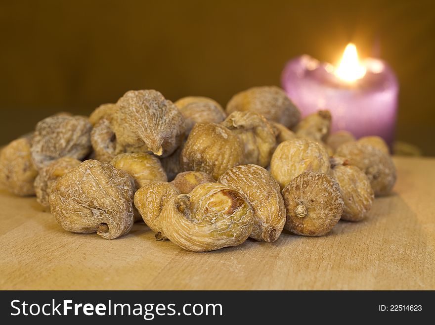 Dried figs on a wooden board with a purple candle in the background