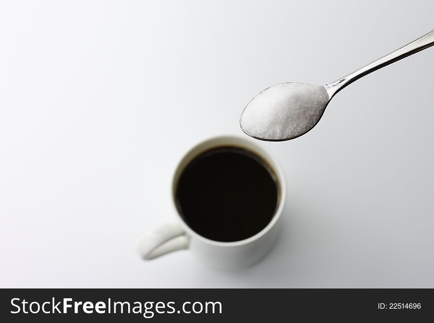 A cup of black coffee and spoonful of sugar on white background.