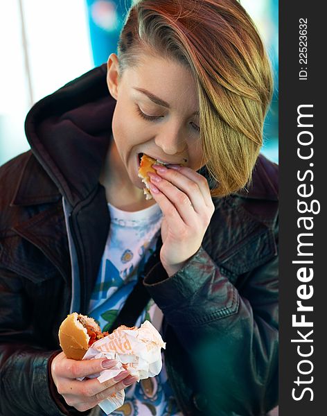 Portrait of stylish blond girl with eats burger on the terrace of the fast food. Portrait of stylish blond girl with eats burger on the terrace of the fast food