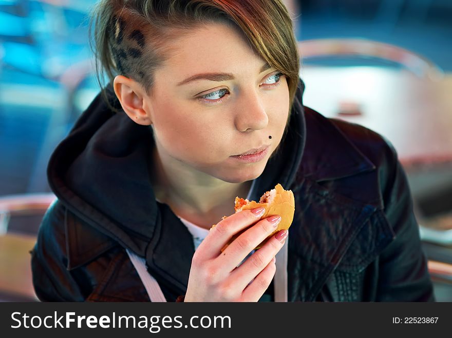 Portrait of stylish blond girl with eats burger on the terrace of the fast food. Portrait of stylish blond girl with eats burger on the terrace of the fast food