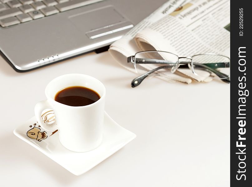 Coffee cup with laptop, glasses and newspaper