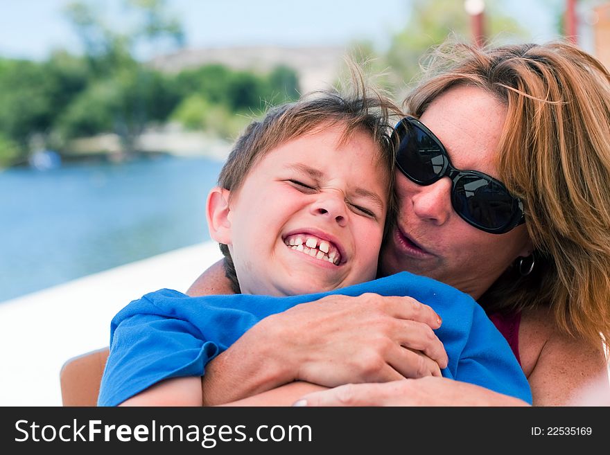 An older mother or young grandmother holds an 8 year old boy on her lap and pretends to kiss him. Boy is laughing hysterically with a huge smile. Image taken outdoors. An older mother or young grandmother holds an 8 year old boy on her lap and pretends to kiss him. Boy is laughing hysterically with a huge smile. Image taken outdoors.