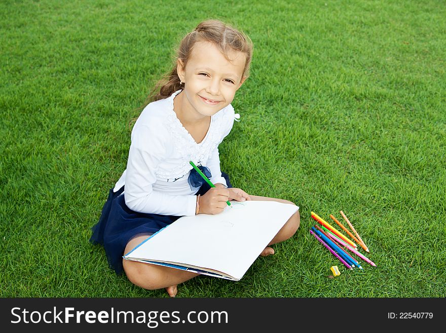 Little cute girl drawing with crayons sitting on a green lawn