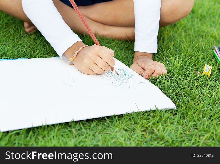 Little cute girl drawing with crayons sitting on a green lawn