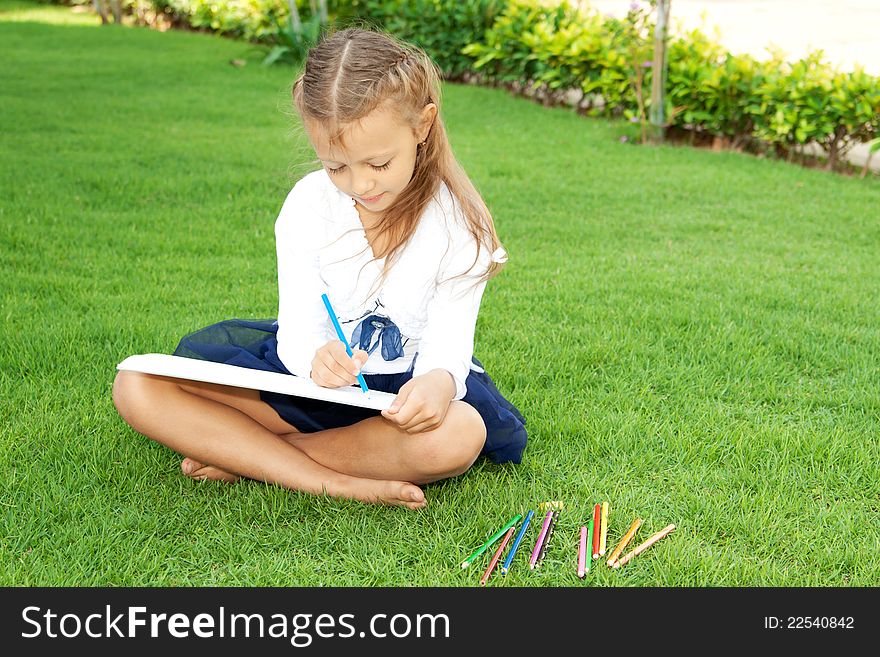 Little cute girl drawing with crayons sitting on a green lawn