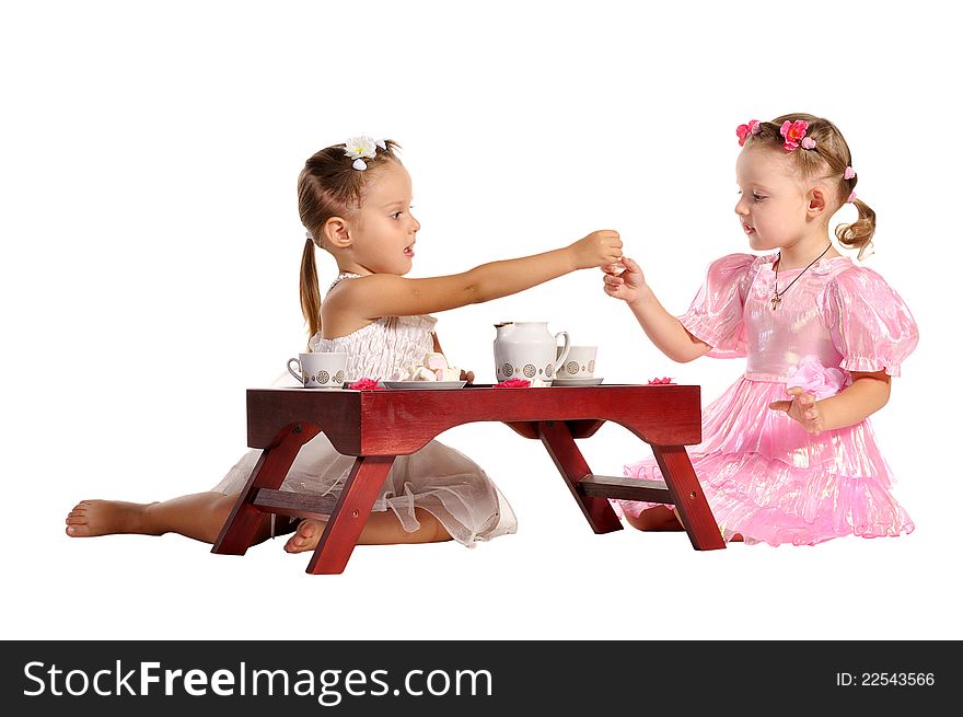 Two pretty twins sisters in beautiful dresses having tea wtih zephyr sitting at coffee table isolated on white background. Two pretty twins sisters in beautiful dresses having tea wtih zephyr sitting at coffee table isolated on white background